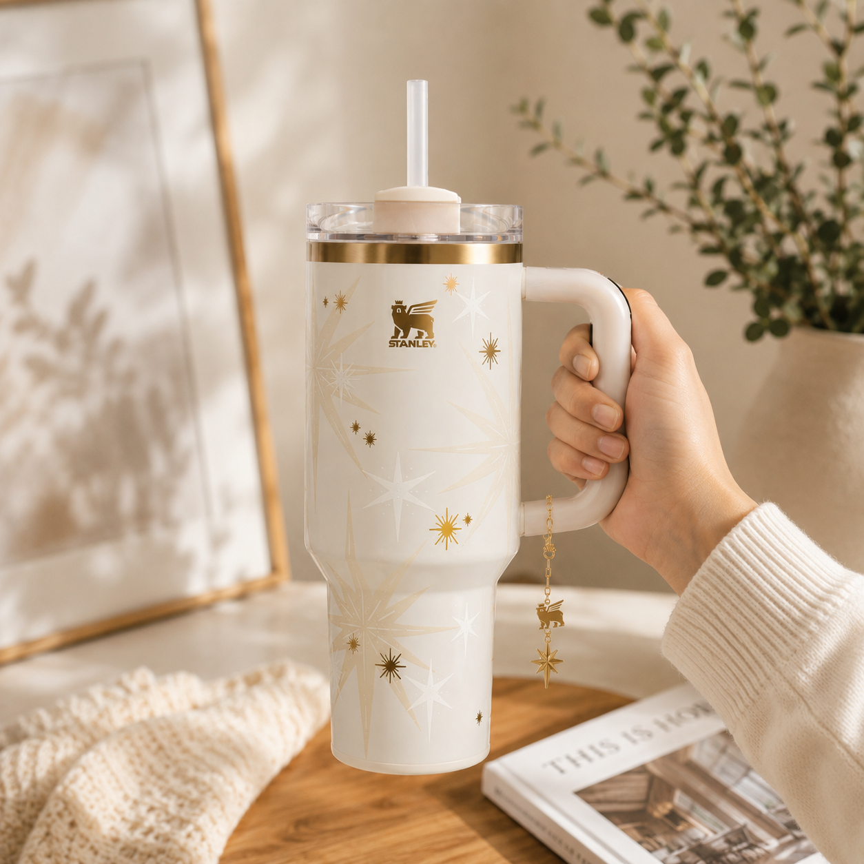 Hand holding a white Stanley tumbler with gold accents on a wooden surface.
