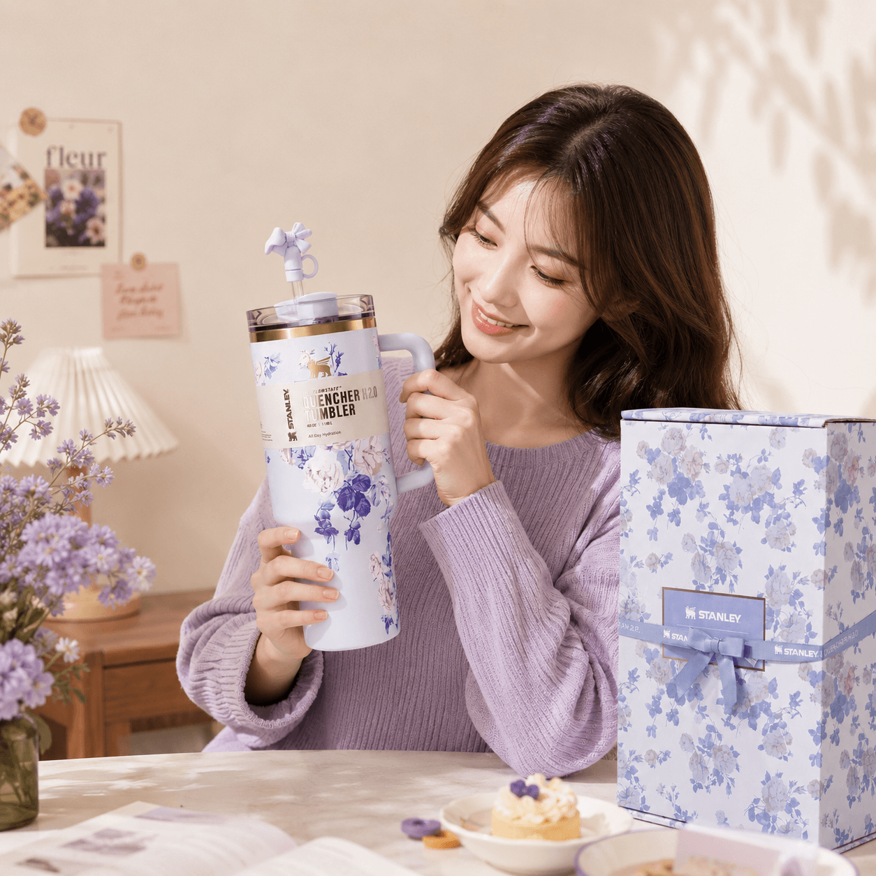 Woman holding a floral-patterned tumbler with a matching box in a cozy indoor setting.