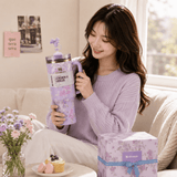 Woman holding a purple tumbler with floral design in a cozy living room.