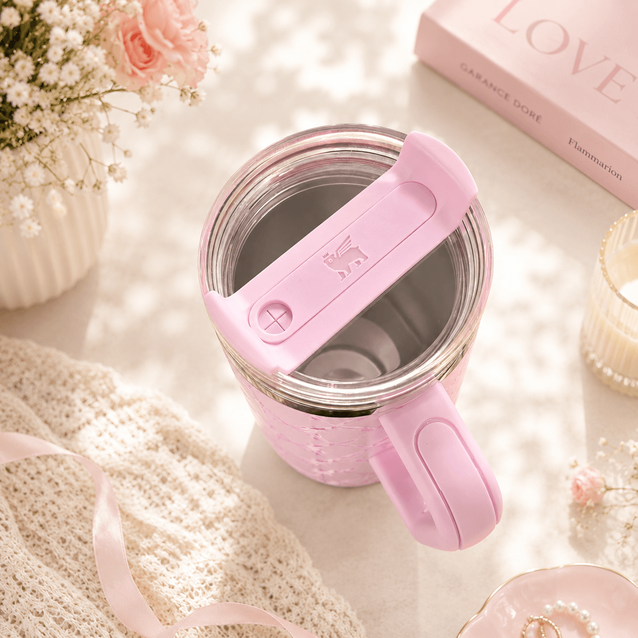 Pink mug with handle on a soft surface with flowers and a book in the background